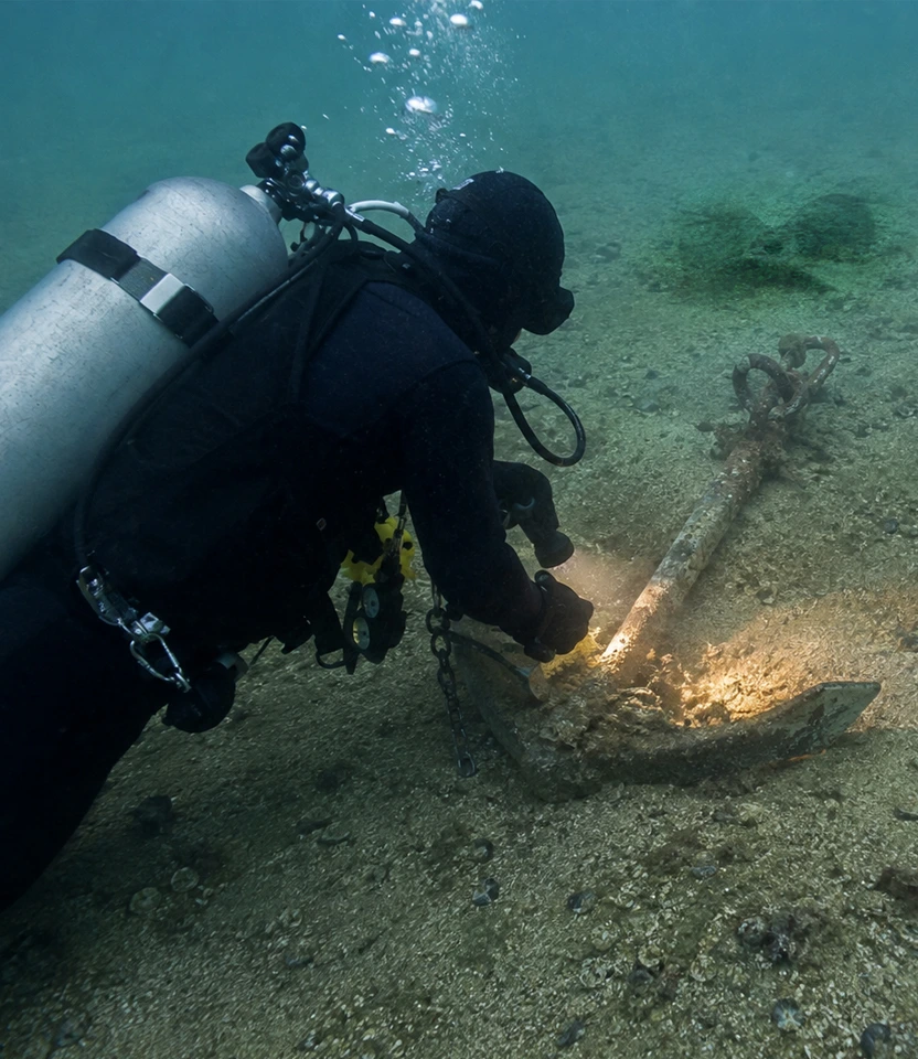 Mergulhador utilizando lanterna subaquática para localizar e recuperar âncora no fundo do mar.