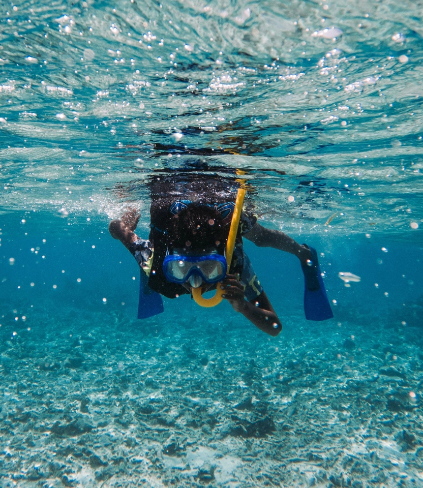 Um casal apaixonado se abraçando e se beijando embaixo d'água enquanto pratica snorkeling no mar azul da Ilha do Xavier, em Florianópolis. Eles estão usando máscaras e nadadeiras.
